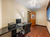 Office space with a desk, computer, printer, and lamp. A black chair faces the desk. The room has wood flooring, beige walls, a window with blinds, and a door with a frosted glass panel.