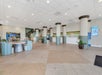 Spacious hotel lobby with beige floor tiles, columns, seating area, potted plants, and a reception desk.
