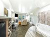 Spacious hotel room featuring a seating area, fireplace, wall-mounted TV, desk, kitchenette, and in-room jacuzzi tub, with large windows and sliding doors to a balcony.