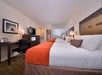 Two queen beds, a flat-screen TV, and a work desk inside a guest room.