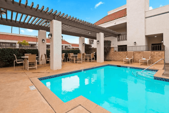 Outdoor heated pool with patio chairs and tables.