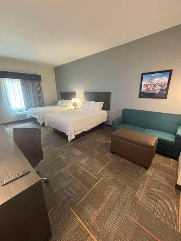 Hotel room with two double beds, a green sofa, a small ottoman, a work desk with a chair, and a window. A mounted picture decorates the gray wall.