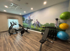 A gym room with exercise equipment, including stationary bikes, a bench, weights, and exercise balls, features a wall mural of people playing golf.