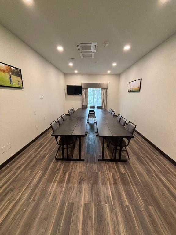 A rectangular conference room with a long table and twelve chairs. There is a wall-mounted TV and framed pictures on the walls. The floor is wood-paneled.