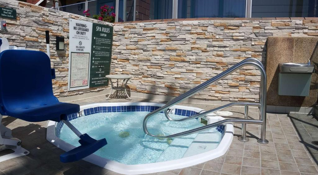Small outdoor spa with a water lift chair, metal handrails, and stone walls. Safety and spa policy signs are visible in the background.