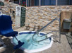 Small outdoor spa with a water lift chair, metal handrails, and stone walls. Safety and spa policy signs are visible in the background.