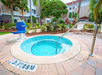 Circular outdoor hot tub with metal handrail, pool lift chair, and depth marker reading "3½ FT 0.9M," surrounded by lounge chairs, plants, and nearby buildings.
