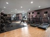 A modern gym with treadmills, exercise bikes, weights, and fitness balls. Mirrors cover one wall, and the flooring is a mix of wood and gym mats.