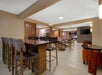 Spacious, modern dining area with wooden floors, high tables, padded stools, regular tables, chairs, and a mounted TV on the wall. Warm lighting and partitions add a cozy ambiance.