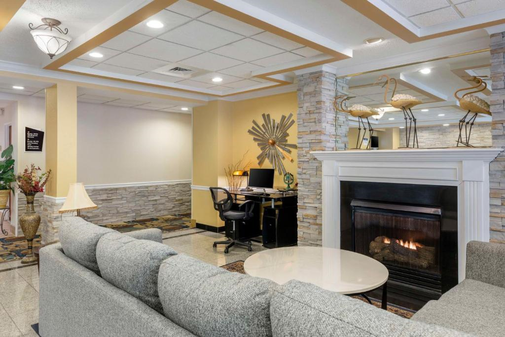 Hotel lobby with a gray sofa, round table, computer desk, and a fireplace. Decorative flamingos on mantel and abstract wall art are visible.