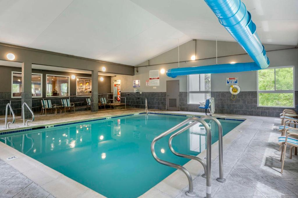Indoor swimming pool with safety railings, a blue water slide, chairs along the wall, and large windows providing natural light.