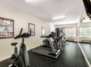 A small gym room features exercise equipment including stationary bikes, treadmills, and a weight machine. Mirrors and posters line the walls.