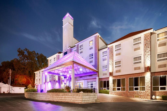 A four-story hotel with a lit entrance and stone accents at dusk.