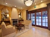 A hotel lobby with a seating area includes two sofas, mirrors, and table lamps surrounding a fireplace. Large chandelier and exit sign overhead. Glass doors lead outside.