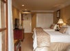 Hotel room with two double beds, beige decor, a TV on a dark wooden dresser, a lamp, and a small table with a chair. A door and a closet are visible in the background.