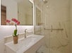 Modern bathroom with a white marble sink and countertop, a mirror with backlighting, a potted orchid, and a glass-enclosed shower featuring marble walls and a metal handrail.