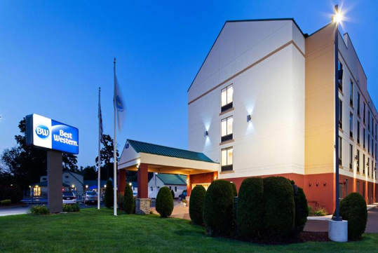 Exterior of a Best Western hotel at dusk, featuring a well-lit entrance, manicured bushes, and a visible hotel sign.