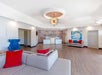 Spacious modern lobby with gray sectional sofa, red and blue cushions, abstract wall art, and a large central light fixture.