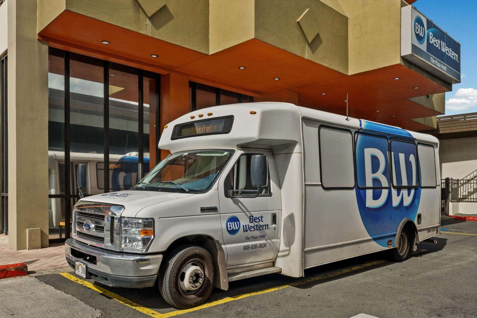 A white Best Western shuttle bus with large "BW" lettering is parked outside a Best Western hotel building.