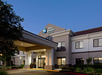 Exterior view of a Best Western Plus Inn & Suites at dusk, featuring a modern entrance, illuminated signage, and surrounding greenery.
