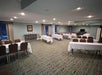 A conference room with tables covered in white cloths and brown chairs arranged in rows, carpeted floor, and soft lighting.