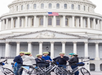 Group of people wearing helmets gather with bicycles in front of the U.S. Capitol, with the American flag visible above.