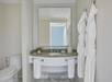 Modern bathroom with a large mirror, granite countertop, sink, and neatly hung white towels and robes. Marble flooring and a closed toilet are visible.