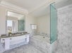 Spacious bathroom with marble bathtub, glass shower, wide mirror above a granite sink, and city view through a large window.