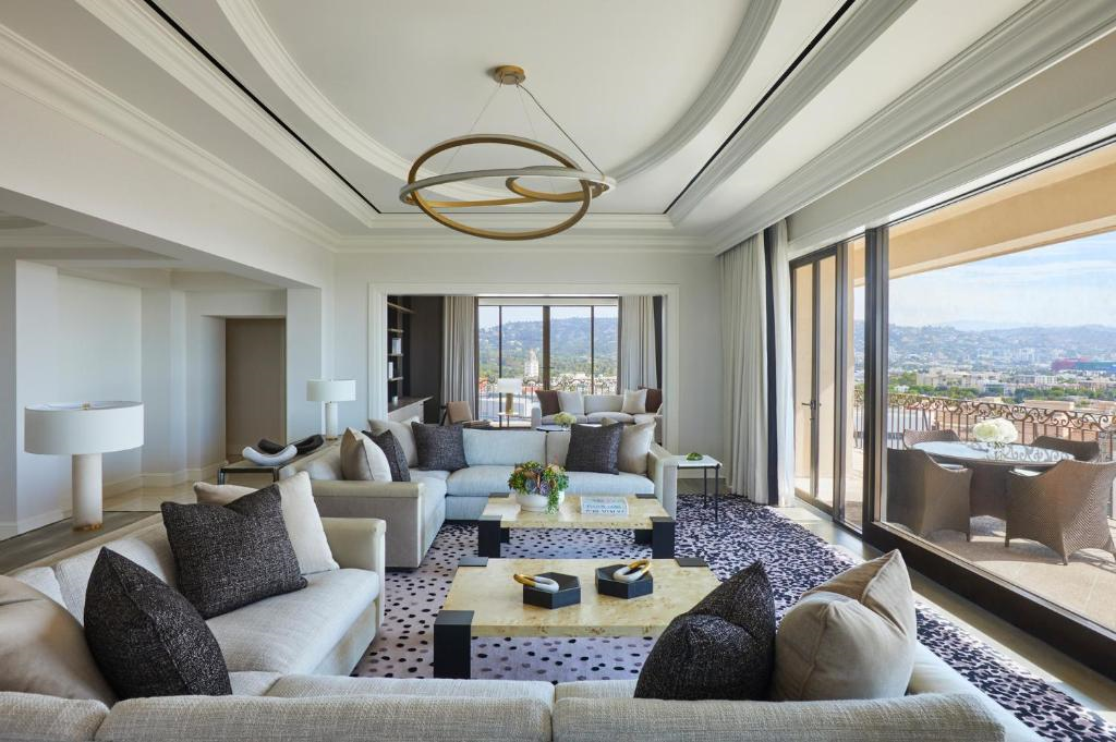 Spacious modern living room with comfortable sofas, a coffee table, and large windows opening to a balcony with scenic views. Neutral tones and abstract decor complete the space.