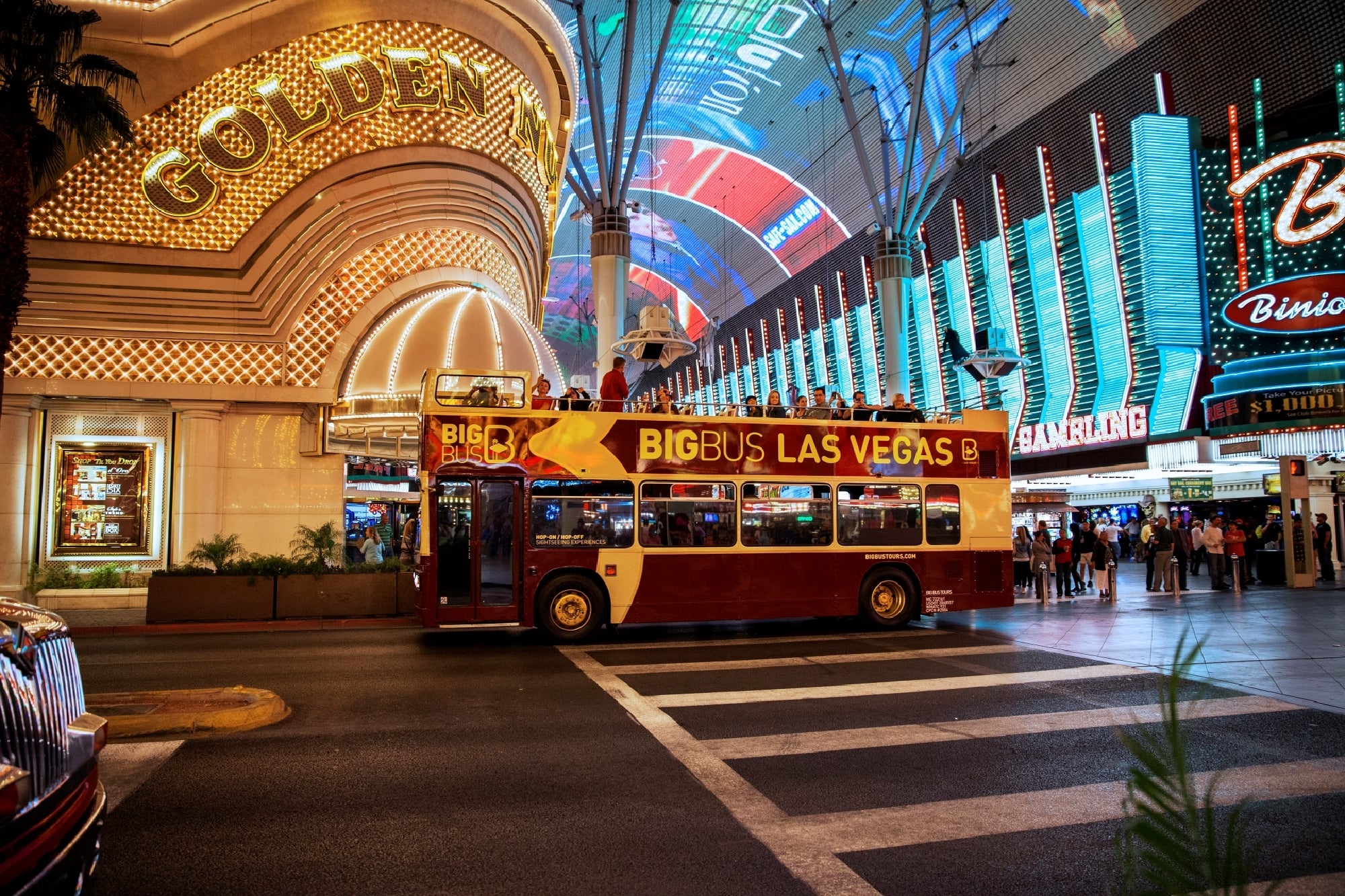 Red double-decker bus labeled "BigBus Las Vegas" on a street with illuminated signs and a casino entrance at night.