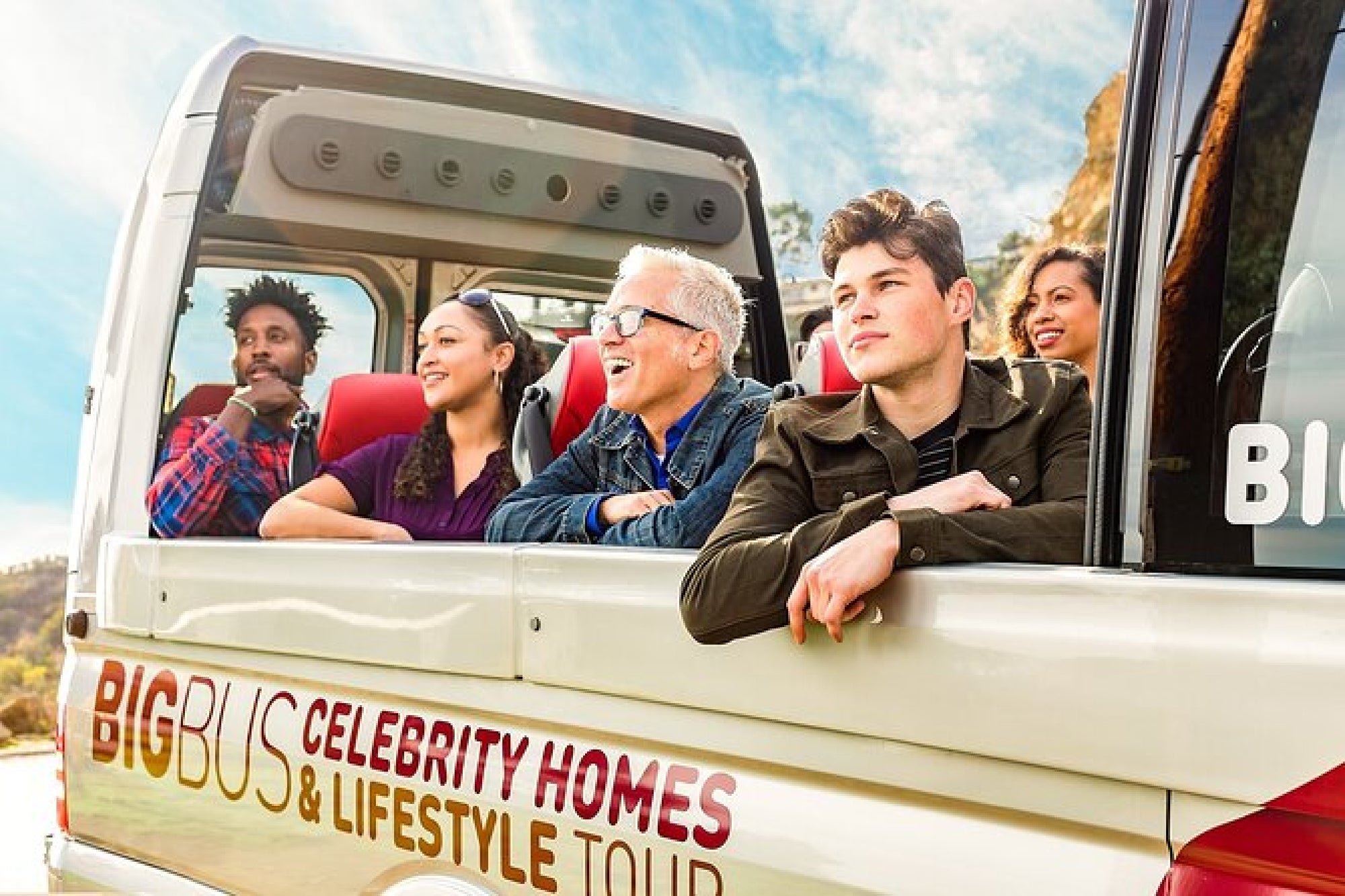 Group of people on an open-top tour bus labeled "Big Bus Celebrity Homes & Lifestyle Tour," looking out and enjoying the view.