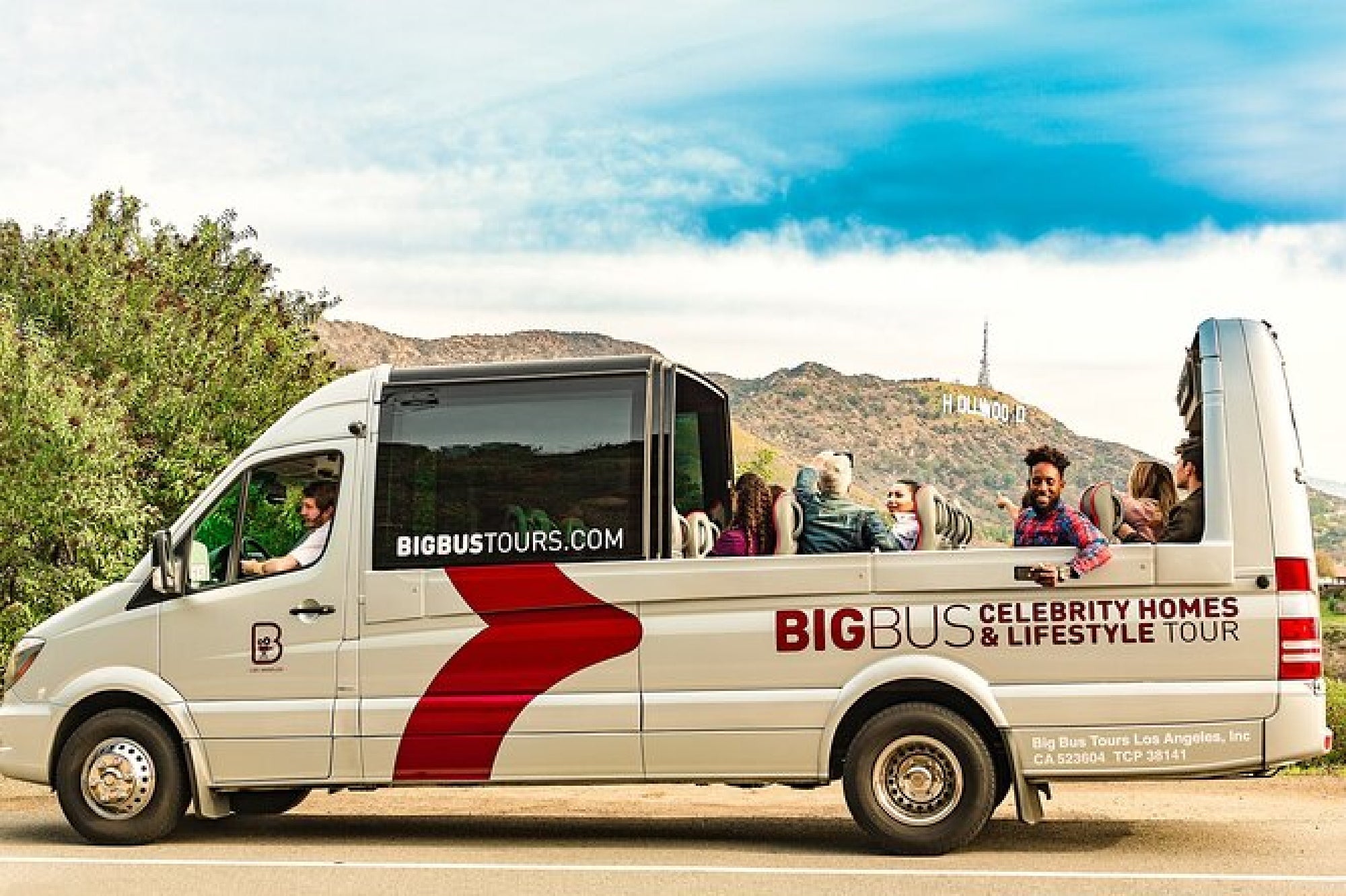 A tour bus with "Big Bus Celebrity Homes & Lifestyle Tour" branding, passengers aboard, and the Hollywood sign visible in the background.