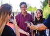 A person holds a small alligator while two smiling people pose for a photo being taken by someone with a phone.