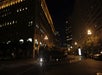 A double-decker tour bus labeled "Big Bus San Francisco" turns a corner on a city street at night, surrounded by tall, illuminated buildings.