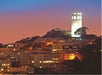 Coit Tower illuminated on top of Telegraph Hill, overlooking residential buildings at dusk in San Francisco.