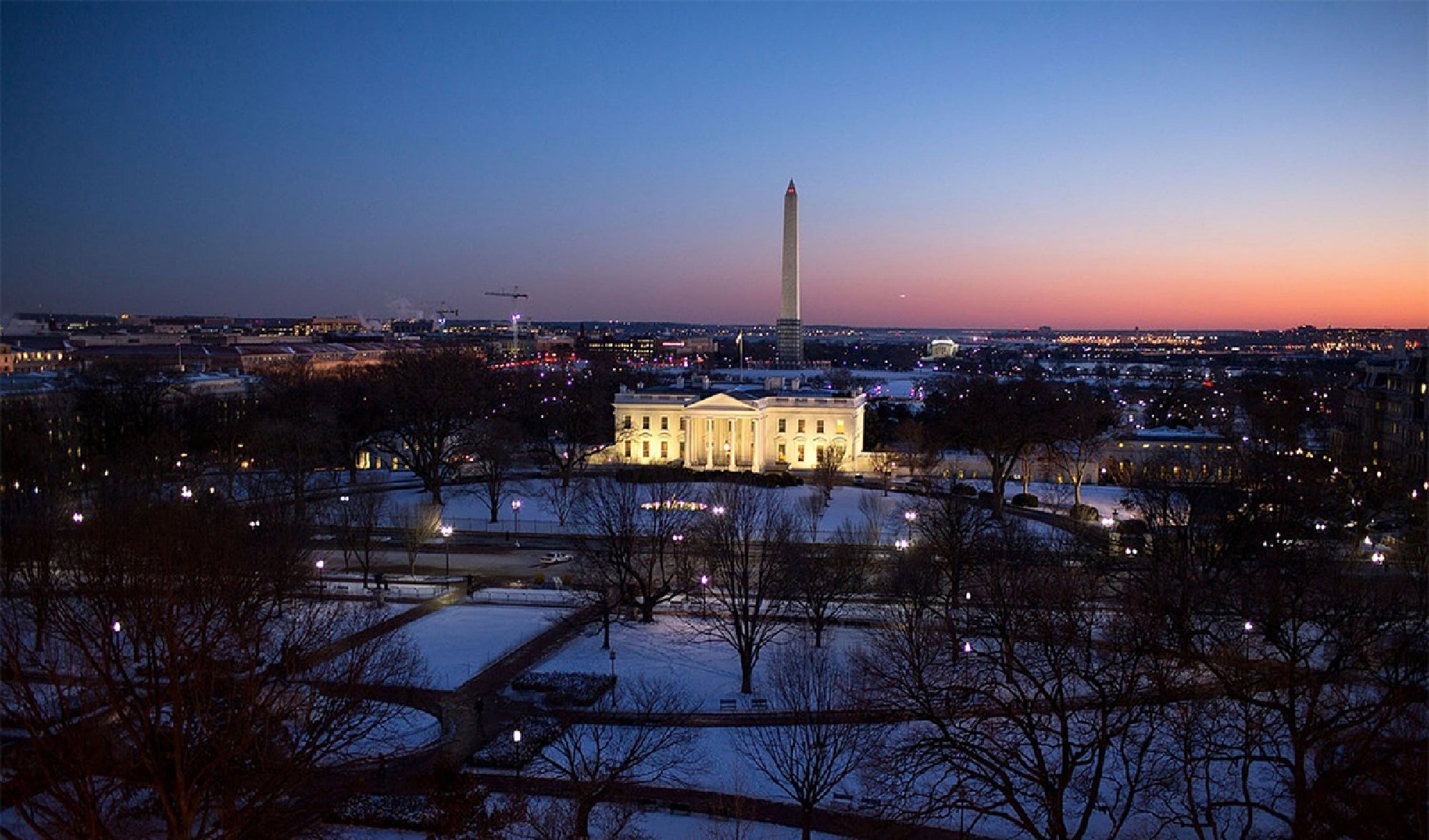 View of the White House and Washington Monument at dusk, surrounded by snow and illuminated by city lights.