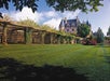 A large, ornate mansion sits behind a manicured lawn with a wooden trellis covered in greenery and trees framing the scene.