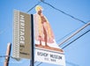 Heritage site sign for Bishop Museum in Hawaii, established 1889, featuring a silhouette of a figure in traditional attire and a blue sky background.
