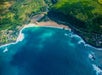 A small cove with blue ocean water crashing against the beach and rocks on the Blue Skies of Oahu Helicopter Tour in Hawaii USA.