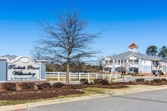 Sign for Parkside Resort Williamsburg, a Bluegreen Resort, with a view of a building and a clear blue sky in the background.