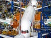 Two commercial airplanes are being assembled inside a large aircraft manufacturing facility, surrounded by platforms, equipment, and workers.