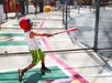 A young boy wearing a red helmet and bright shorts swings a bat at a baseball in a batting cage.