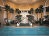 Luxurious indoor pool with surrounding palm trees, a modern sculpture, and a grand staircase in the background.