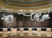 A modern hotel lobby with a long, curved reception desk and abstract, flowing light sculptures hanging from the ceiling.