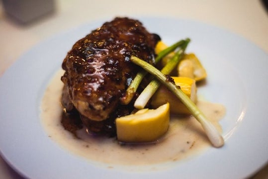 Close up of a plated dinner with a protein in a sauce with vegetables under it and on the side on the Boston Signature Dinner Cruise in Boston.