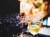 Close up of several glasses of red and white wine and cocktail with lights in the blurred background.