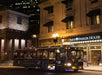 A trolley labeled "Ghosts & Gravestones" passes by the lit exterior of the Omni Parker House at night in an urban setting.