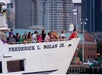 A white cruise ship with it's deck full of people on the Boston Historic Harbor Cruise with the city in the background.