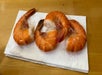 Three cooked shrimp are placed on a white paper napkin, which rests on a wooden surface.