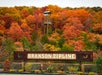 A wooden sign reading "Branson Zipline" stands in front of autumn-colored trees and a tall wooden observation tower.